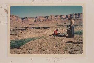 Across Labyrinth Canyon from above mouth of Horsethief Canyon. Road down left bank is at edge of bototom. A. C. Ekker watches Masland at his camera