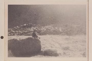 It appears to be Bessie Hyde sitting next to a rapid which flows from left to right. Print owned by Mrs. William Haley and probably one of those made from the films found in the snow