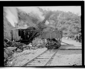 View of the steam shovels working on the reservoir of Kaweah #3 Hydro Plant. showing railway tracks. rocks. and mountains in the background. ca. 1913. (This photo is out of focus. but otherwise. very similar to N-
