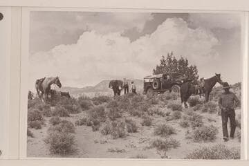 Preparations to leave the truck and take to the pack string. Rainbow Plateau at edge of Navajo Canyon. Nancy and Tom Daly work at the packs. White-hat at right. Navajo Mountain in the distance